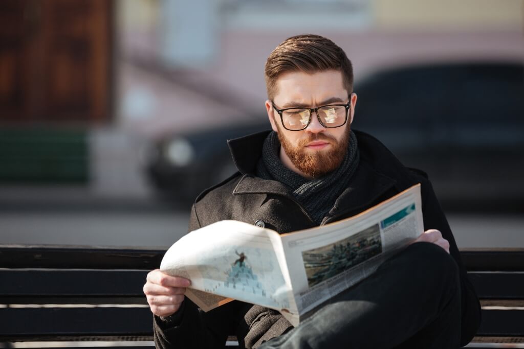 Man sat on a bench reading a newspaper